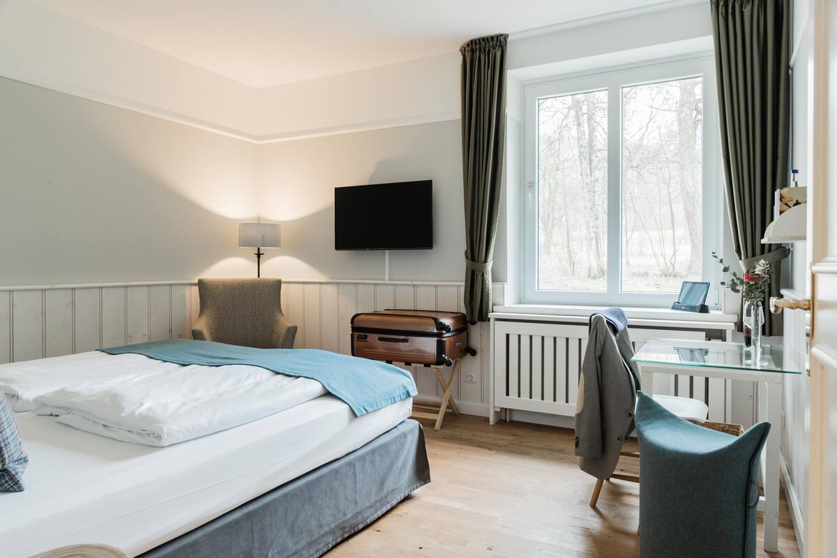 Ein Hotelzimmer mit Bett, Schreibtisch, Stuhl, Fernseher und einem Fenster mit Vorhängen.