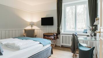 A hotel room with a bed, a desk, a chair, a television, and a window with curtains.