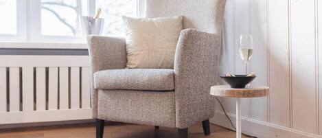 A modern armchair with a cushion, a small round table with a wine glass, and a bowl.