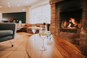 Zwei Gläser Weißwein auf einem Holztisch, im Hintergrund ein Kamin aus Ziegelsteinen.
