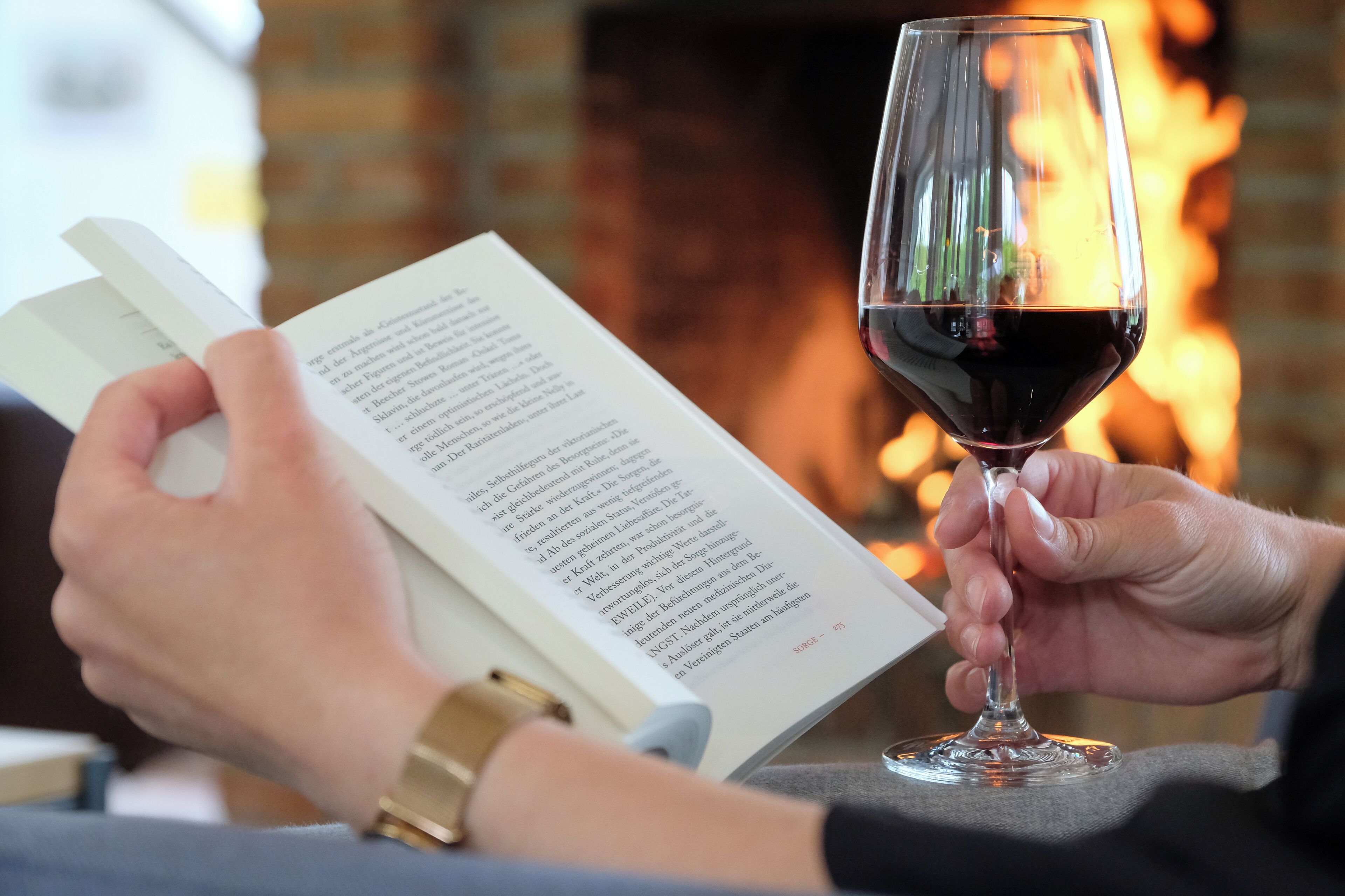 Una persona leyendo un libro con una copa de vino tinto.