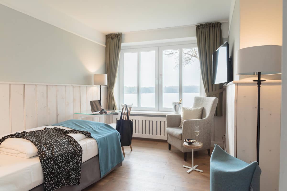 Ein Hotelzimmer mit Bett, Sessel, kleinem Tisch, Fernseher und einem Fenster mit Vorhängen.