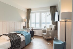 Ein Hotelzimmer mit Bett, Sessel, kleinem Tisch, Fernseher und einem Fenster mit Vorhängen.