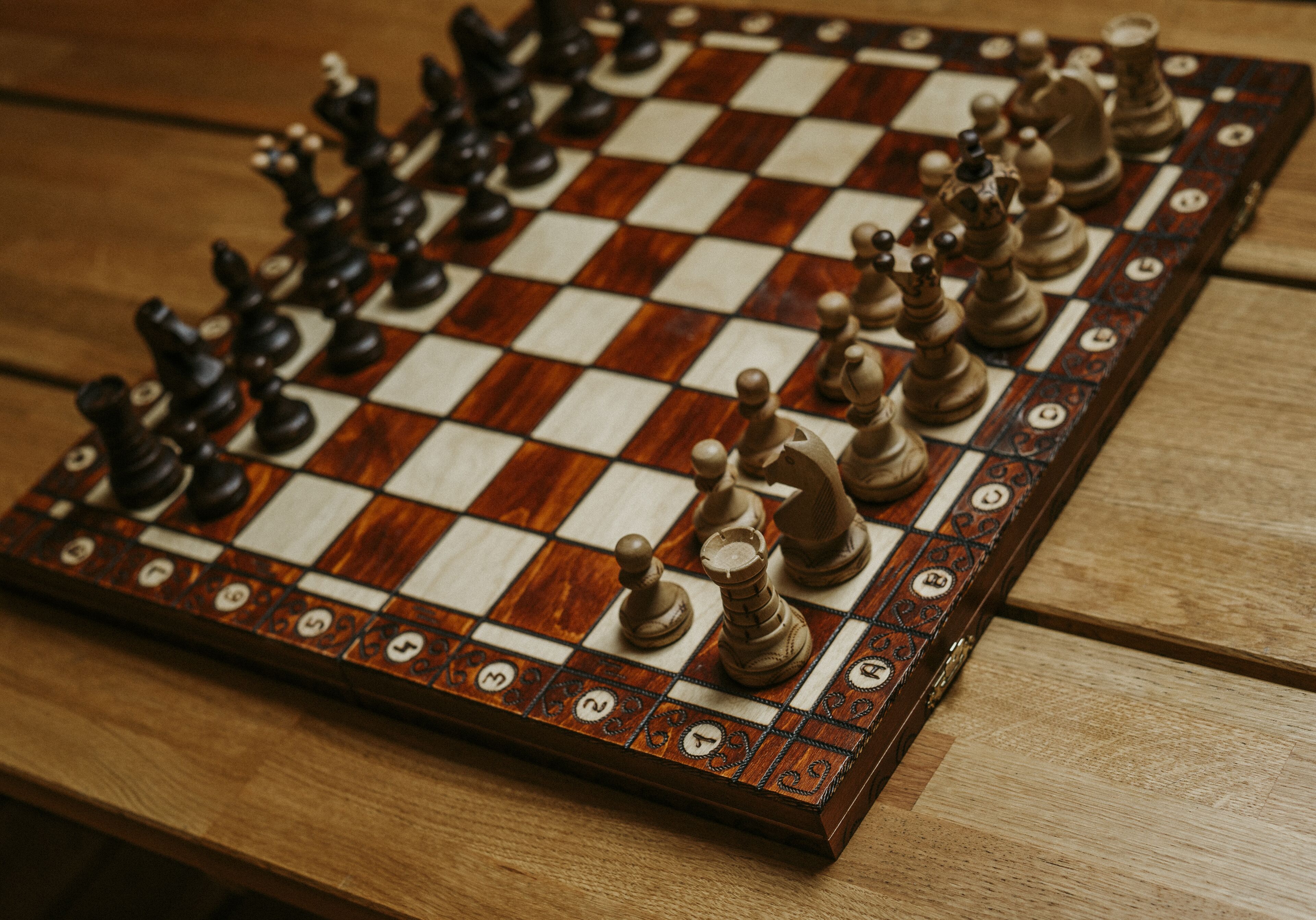 A wooden chessboard with chess pieces on a table.
