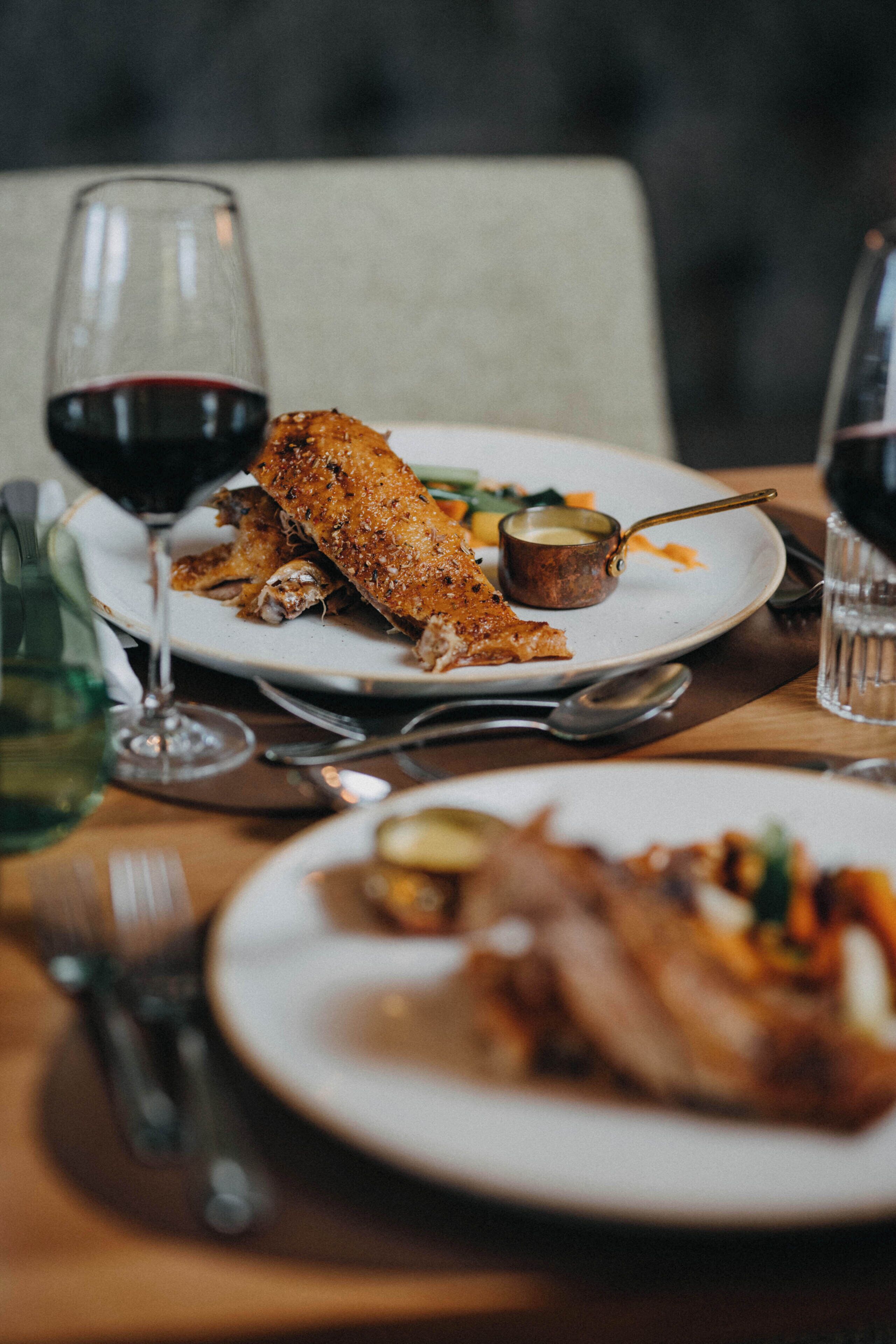 A dining table with plates of food, a glass of red wine, and cutlery.