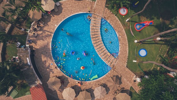 An aerial view of a circular pool with a wooden deck, surrounded by palm trees and umbrellas. - Hotel Kamico (Tapachula)