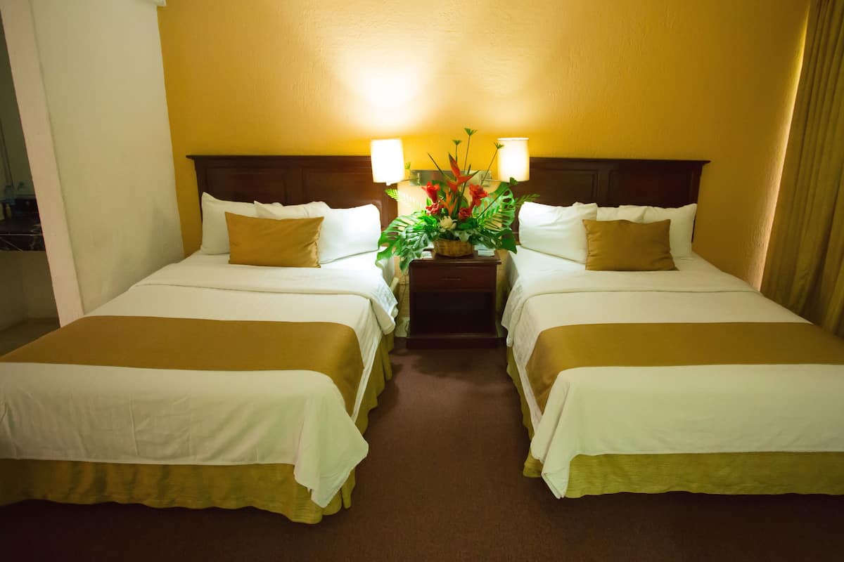 A hotel room with two beds, a nightstand with lamps, and a decorative plant.