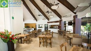 A hotel dining area with wooden tables and chairs, ceiling fans, and a kitchen in the background. - Hotel Kamico (Tapachula)