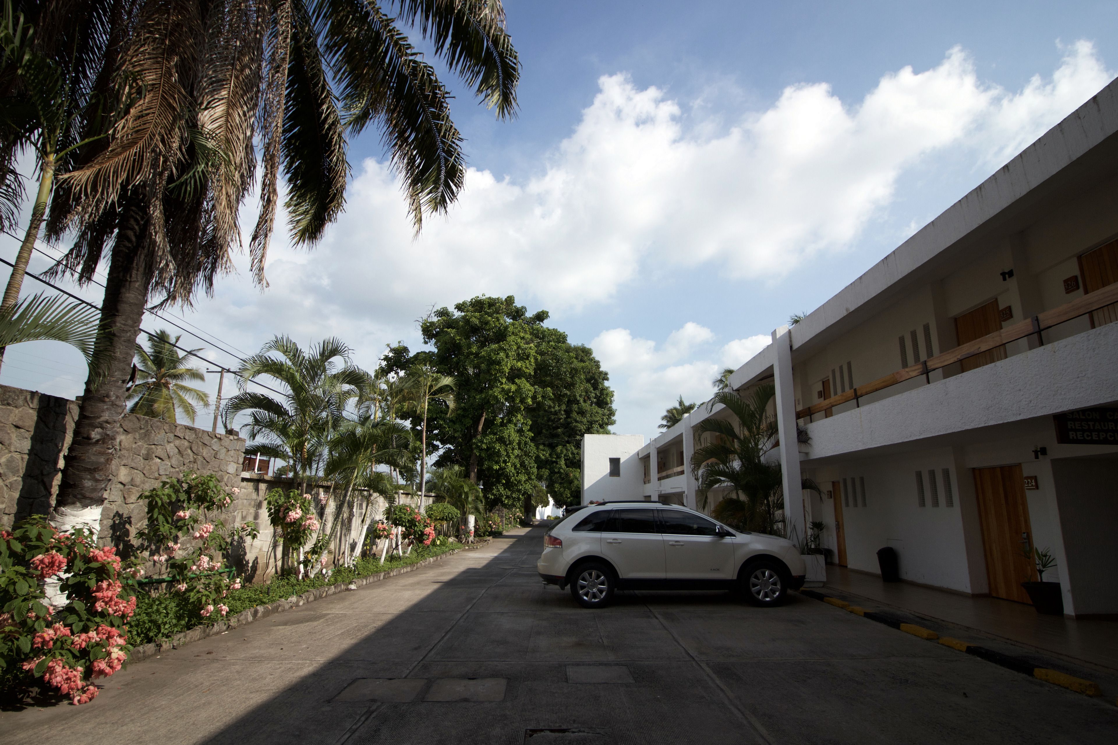 A street view with a parked car, a building with a sign reading "Restroom," and a large tree in the background.