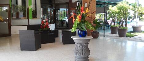 Un área de recepción con una columna de piedra, muebles de mimbre y plantas en macetas.
