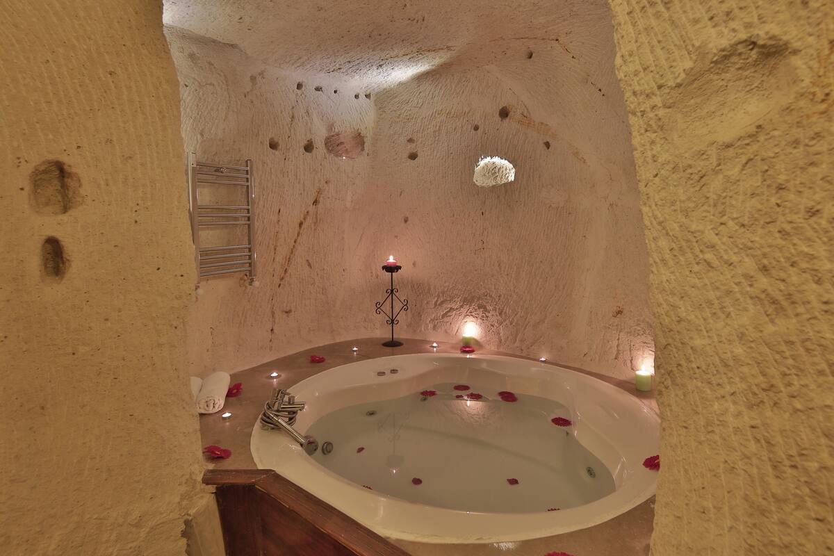 Ein Spa-Raum mit einer großen Badewanne, gefüllt mit Wasser und Rosenblättern, einer kleinen Kerze und einem Handtuchhalter.