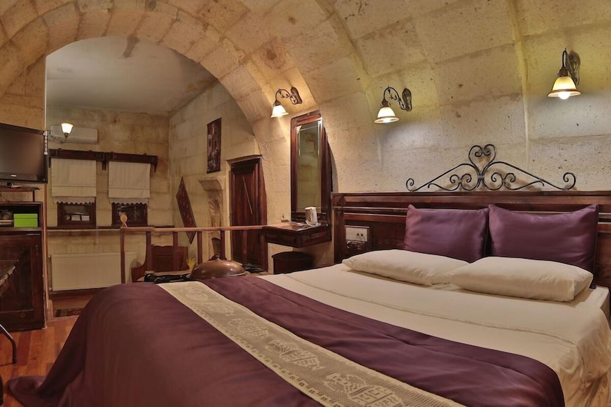 A room with a bed, wooden headboard, and two wall-mounted lamps.