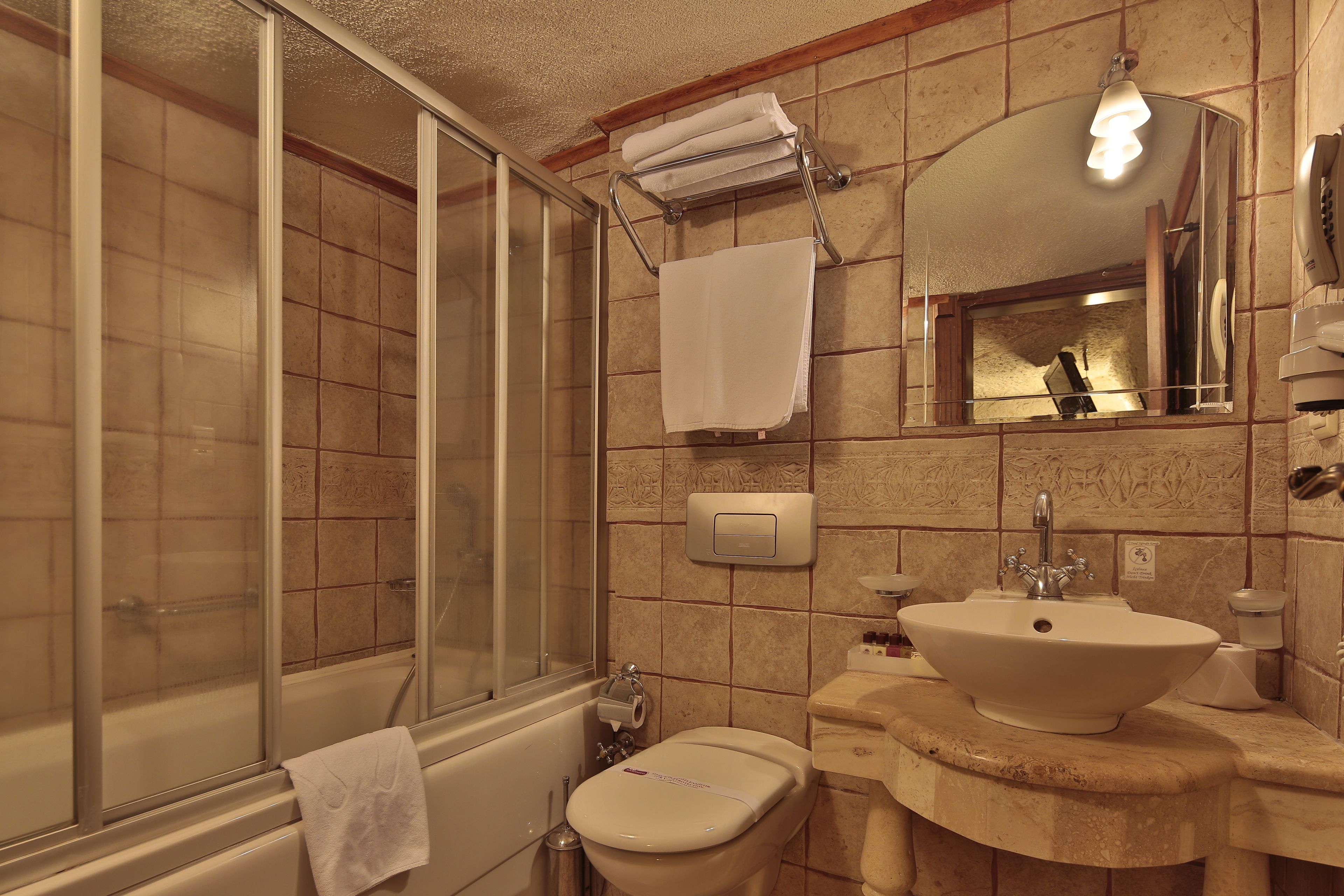 A bathroom with a glass-enclosed shower, a toilet, and a sink with a mirror above it.