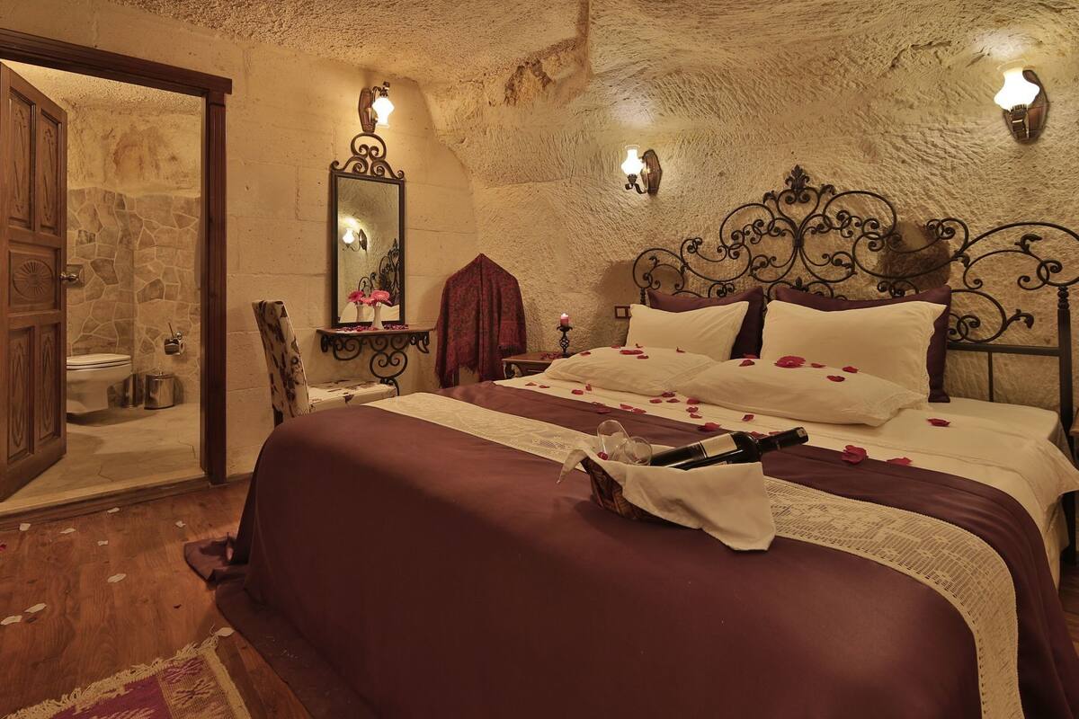 Ein Schlafzimmer mit einer Steinwand, einem Bett mit Rosenblättern, einem Spiegel und einem Nachttisch mit einer Kerze.