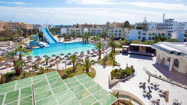 A resort with a large swimming pool, a water slide, and multiple sun loungers.