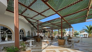 An outdoor patio area with tiled flooring, outdoor seating, and a covered section with a metal and green net roof.