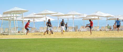 A beach volleyball game with players and spectators under white umbrellas.