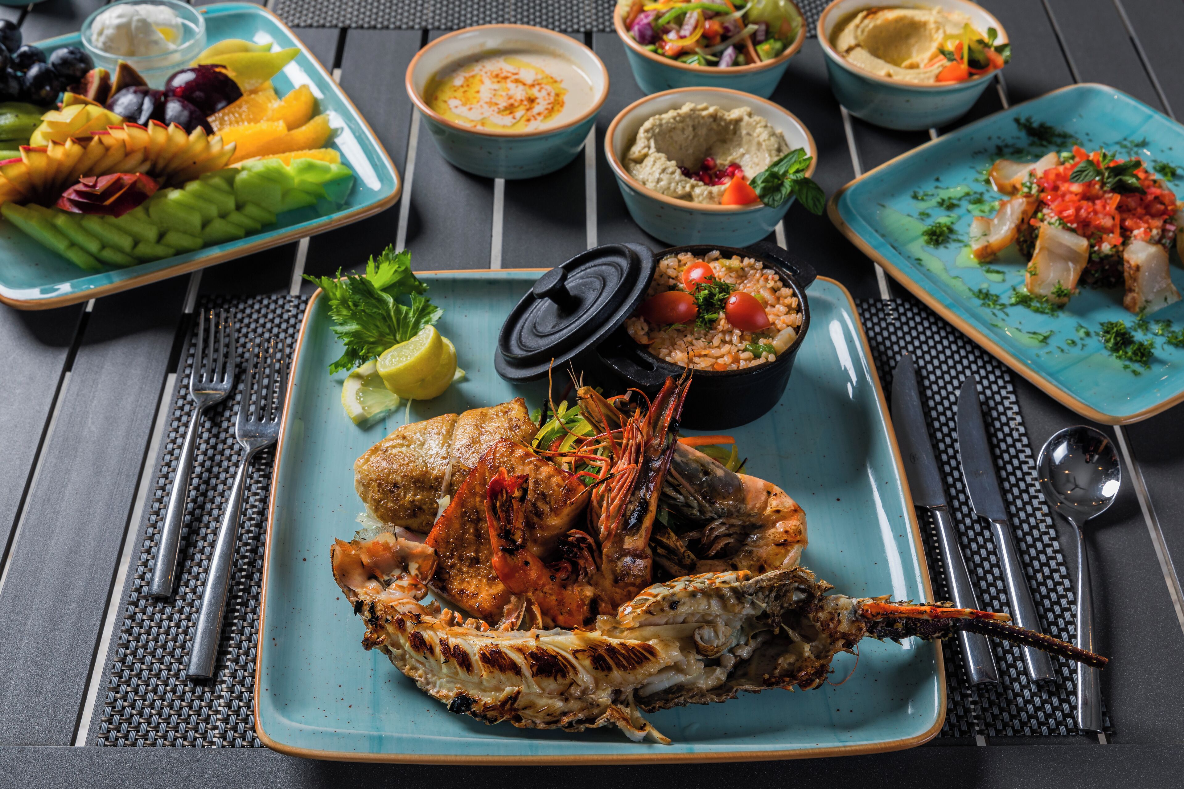 Una bandeja de mariscos con camarones y langosta a la parrilla, acompañada de diferentes guarniciones y salsas.