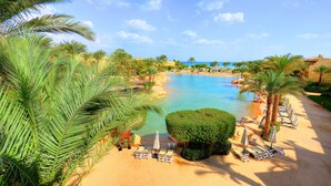 Een resort met een groot zwembad, palmbomen en ligbedden.