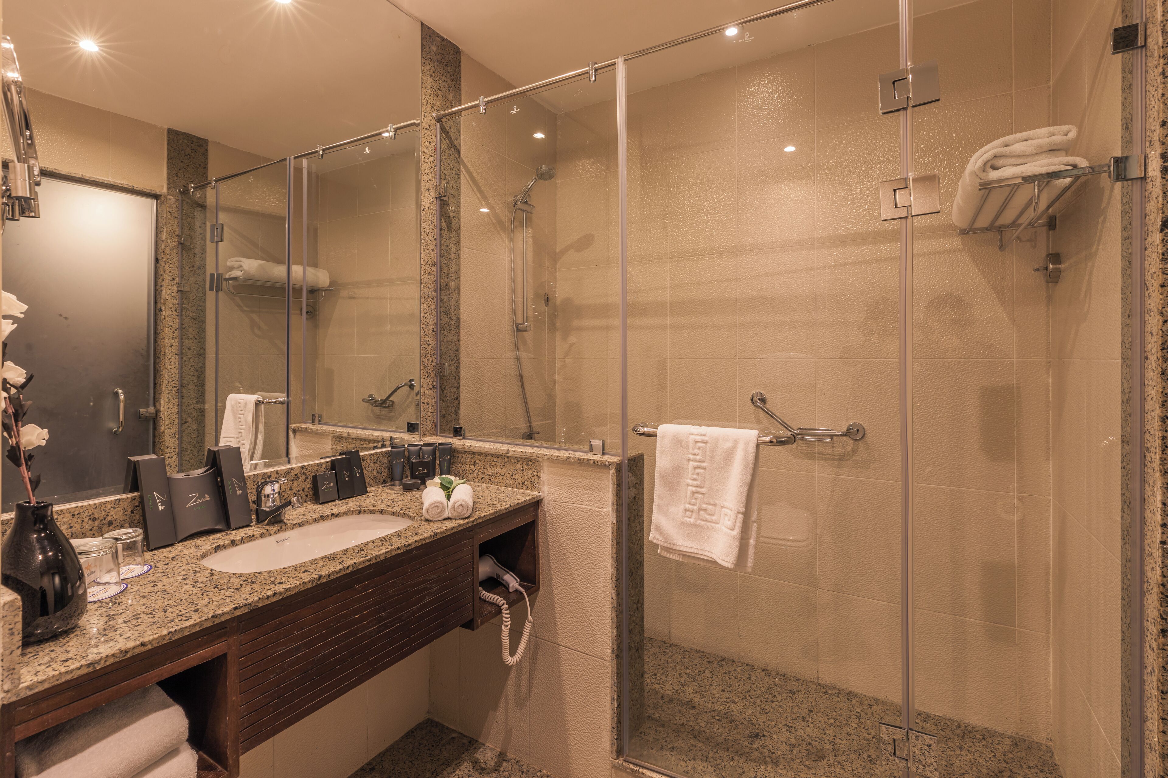 Un bagno moderno con un piano di lavoro in granito, un lavabo, uno specchio, uno spazio doccia in vetro e un portascope.