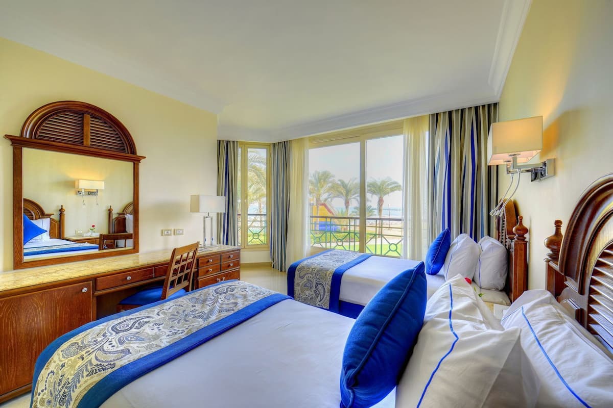 Une chambre d’hôtel avec deux lits, un bureau, une chaise, un grand miroir et un balcon avec vue.