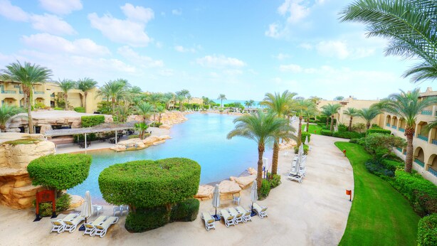 Een resort met een groot zwembad, palmbomen en ligbedden.