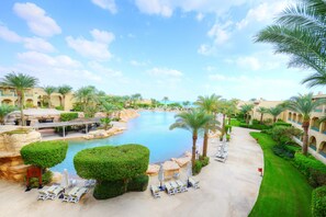 Een resort met een groot zwembad, palmbomen en ligbedden.