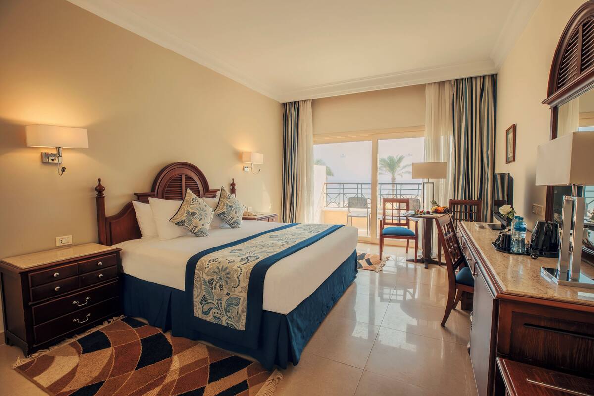 Une chambre d’hôtel avec un grand lit, un bureau, une chaise, une commode et un balcon avec vue.