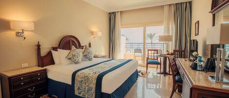 A hotel room with a large bed, a desk, a chair, a dresser, and a balcony with a view.