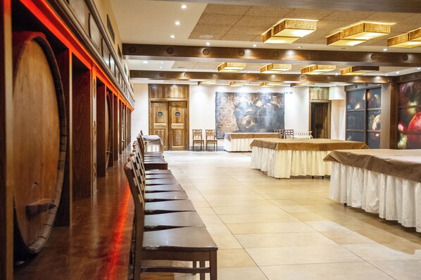Un amplio salón de banquetes con largas bancas de madera, mesas con manteles blancos y un mural grande en la pared de fondo.