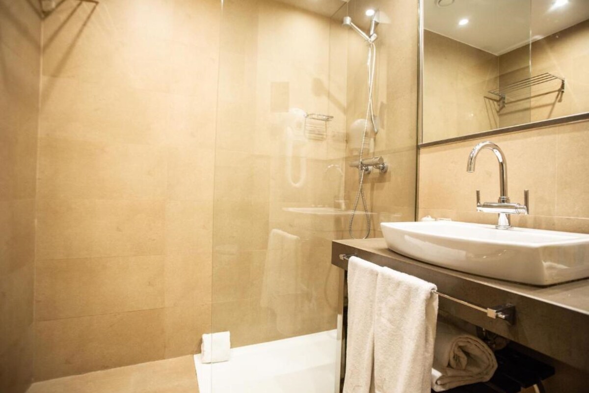 Un baño moderno con ducha envuelta en vidrio, un lavabo blanco y un espejo encima.