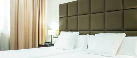 A hotel room with a large bed, a headboard with a padded design, a nightstand with a lamp, and a window with curtains.