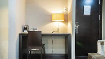 Quarto de hotel com escrivaninha, cadeira, luminária e porta com fechadura e placa.