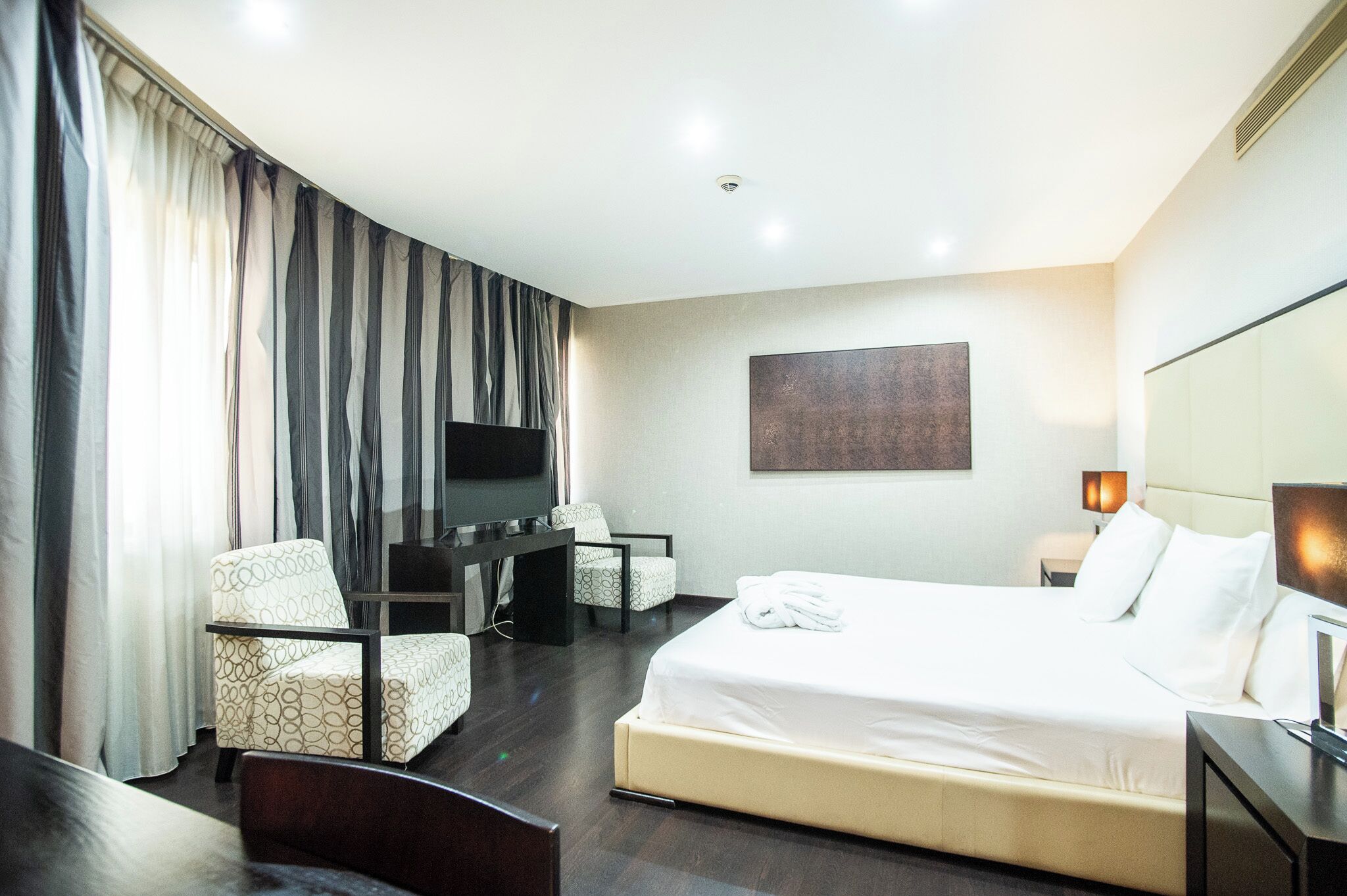 Habitación de hotel con cama, dos sillones, escritorio, televisor y un cuadro en la pared.