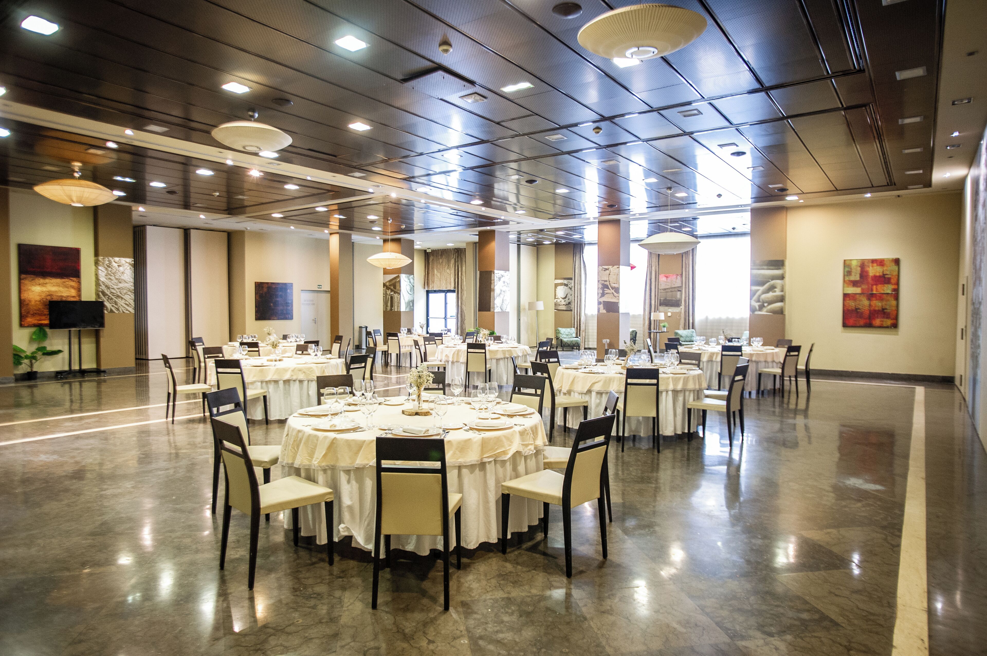 Un amplio salón de banquetes con mesas redondas dispuestas para cenar, equipado con sillas y vajilla.