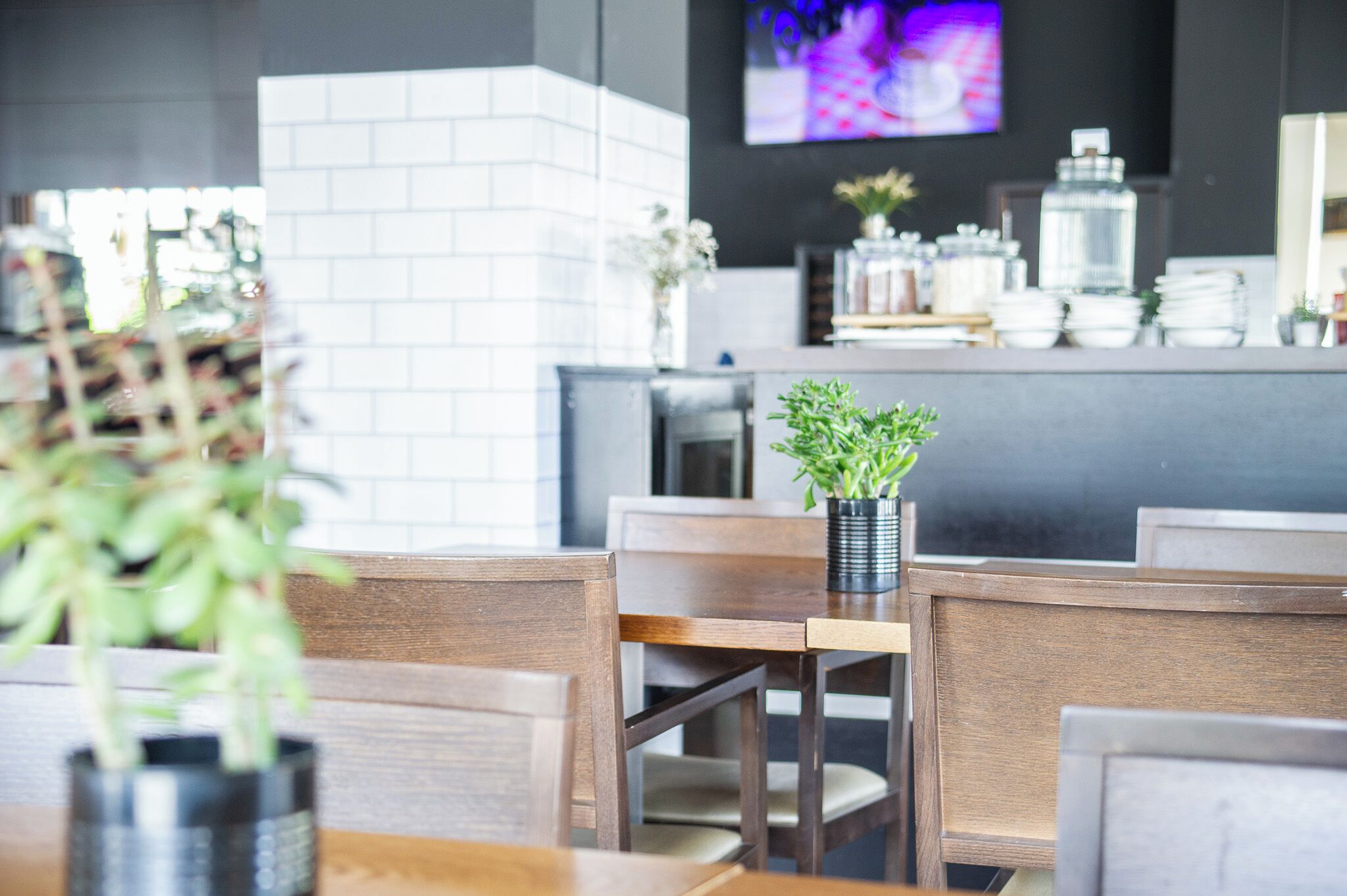 Een restaurantinterieur met houten tafels en stoelen, een bakstenen muur en een televisiescherm op de achtergrond.