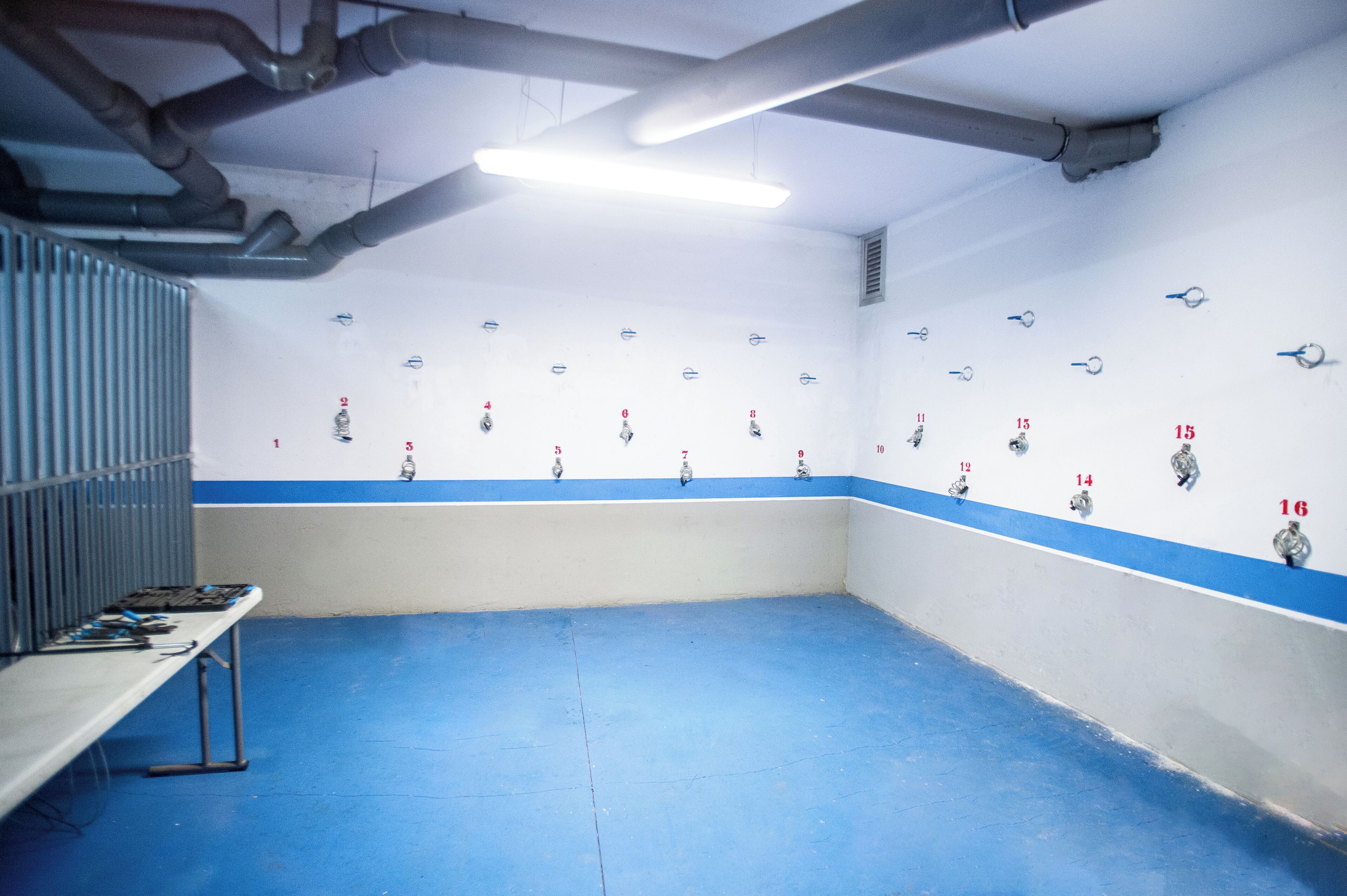 A room with numbered lockers, a metal bench, and a blue floor.