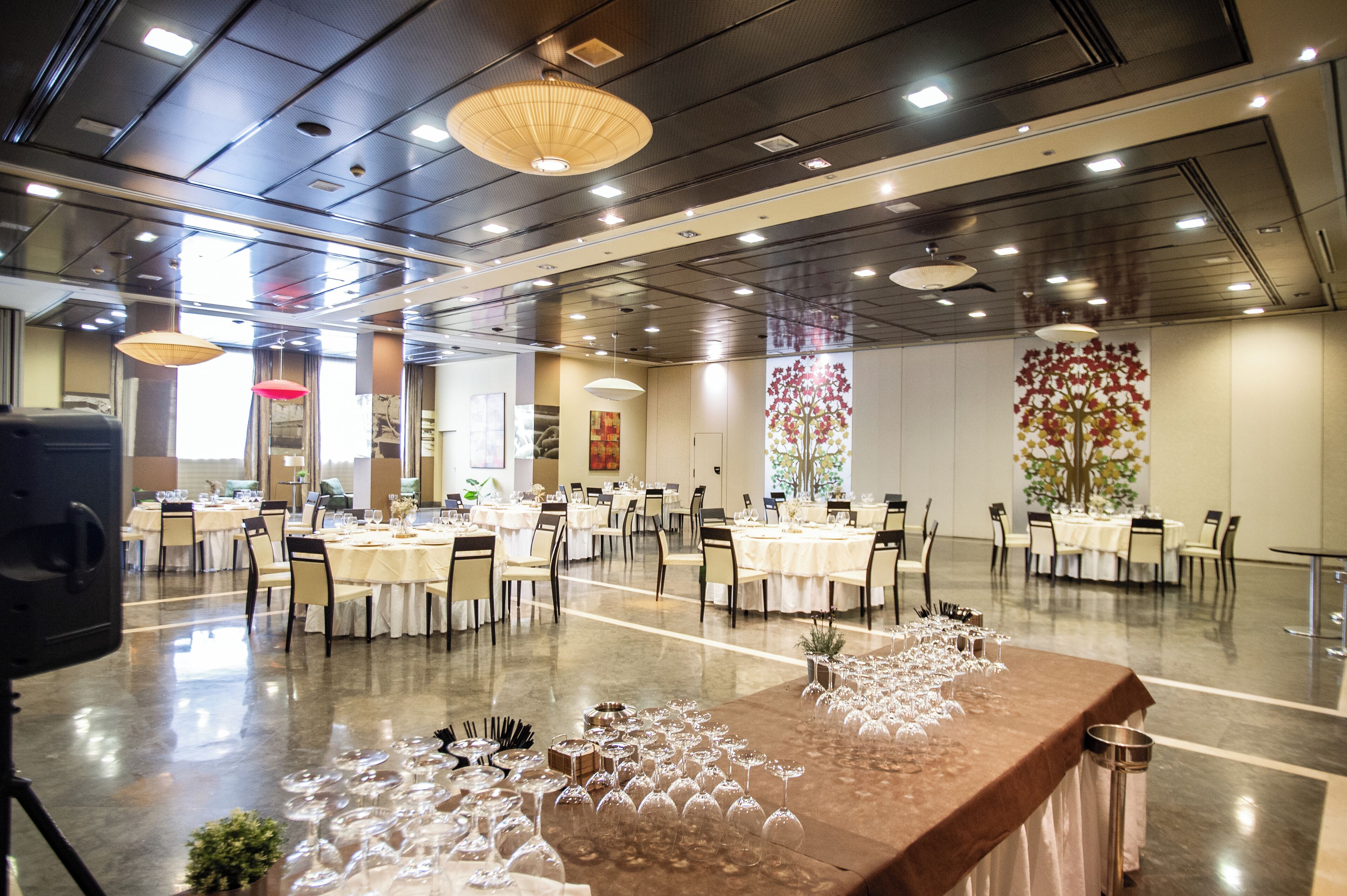 A spacious banquet hall with multiple round tables set for dining, a central floral arrangement, and a modern ceiling design.