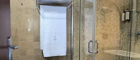 A glass-enclosed shower with a tiled floor and walls, a towel rack with a folded towel, and a door with a handle.
