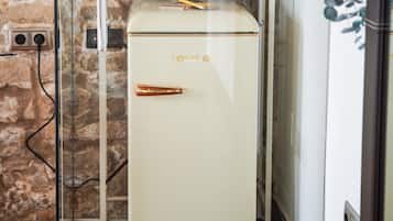 A vintage refrigerator with a shelf above it holding jars and glasses.