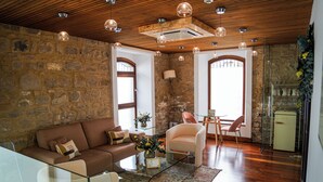 A living room with a stone wall, wooden ceiling, and a glass coffee table. - Hotel Baeza Monumental by eme Hoteles (Baeza)