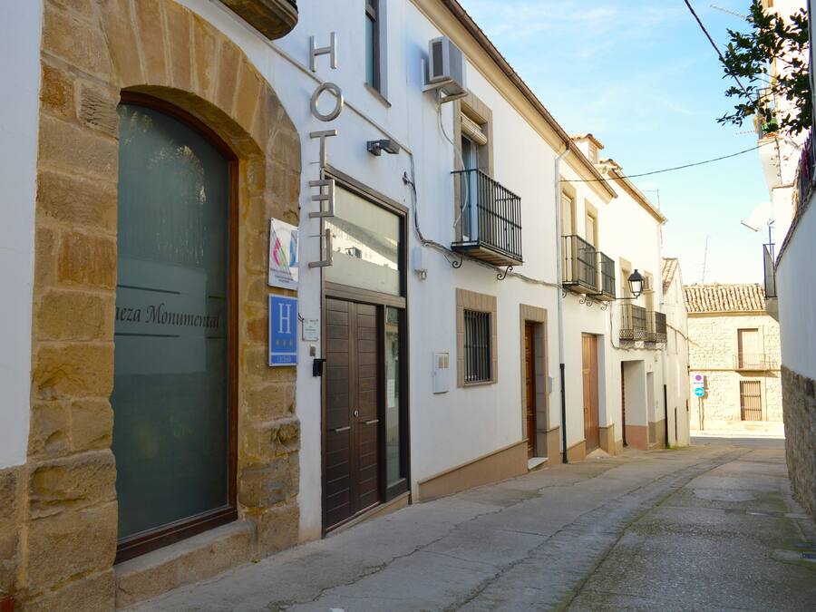 Una calle estrecha con un hotel a la izquierda, que presenta fachada de piedra, un gran ventanal de arco y un cartel que indica un museo.