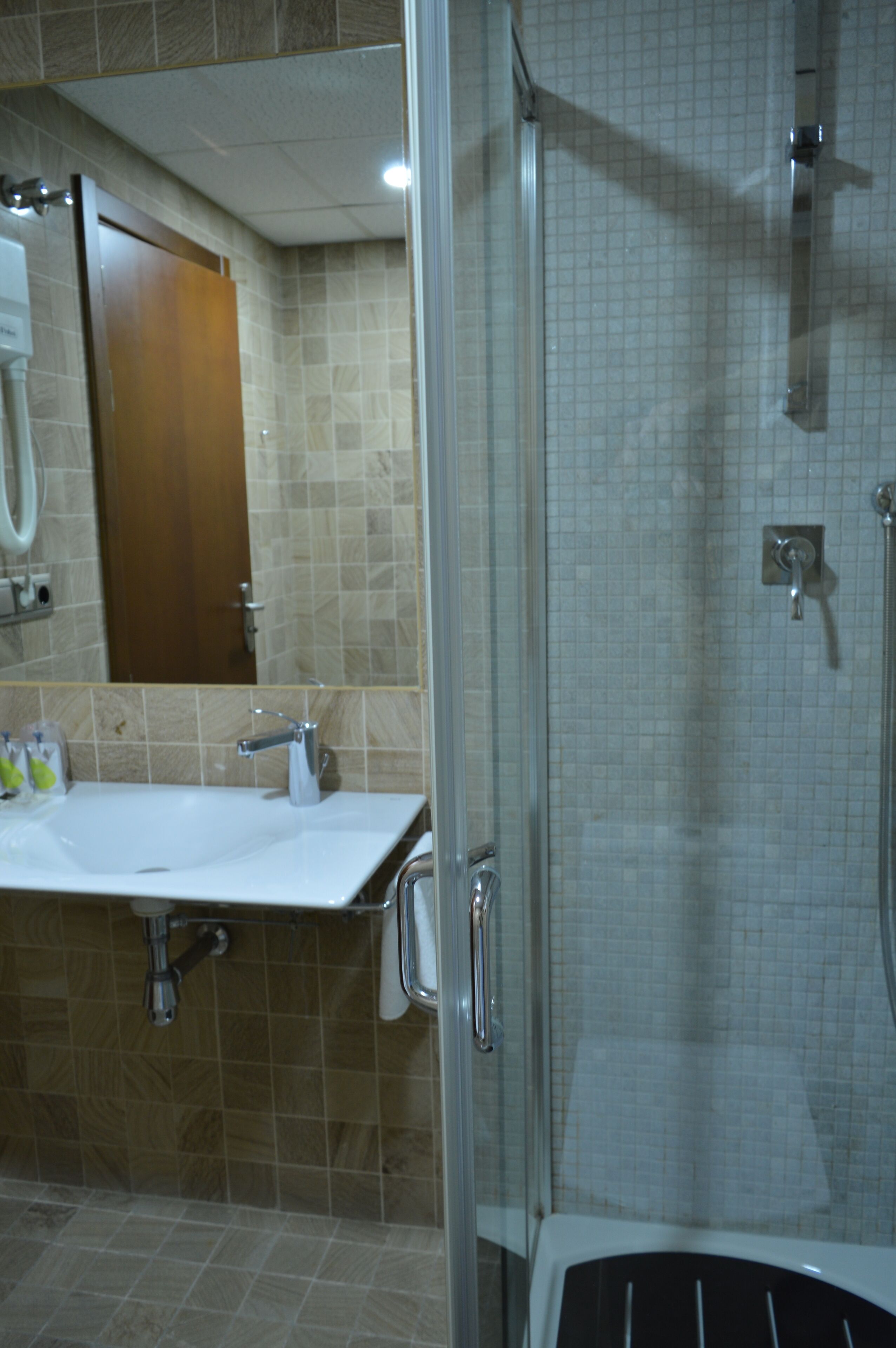 Un bany amb dutxa de vidre, un lavabo amb mirall i un suport per a tovalloles.