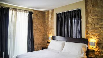 Camera d'albergo con parete in pietra, un letto con lenzuola bianche, un comodino con una lampada e un telefono.