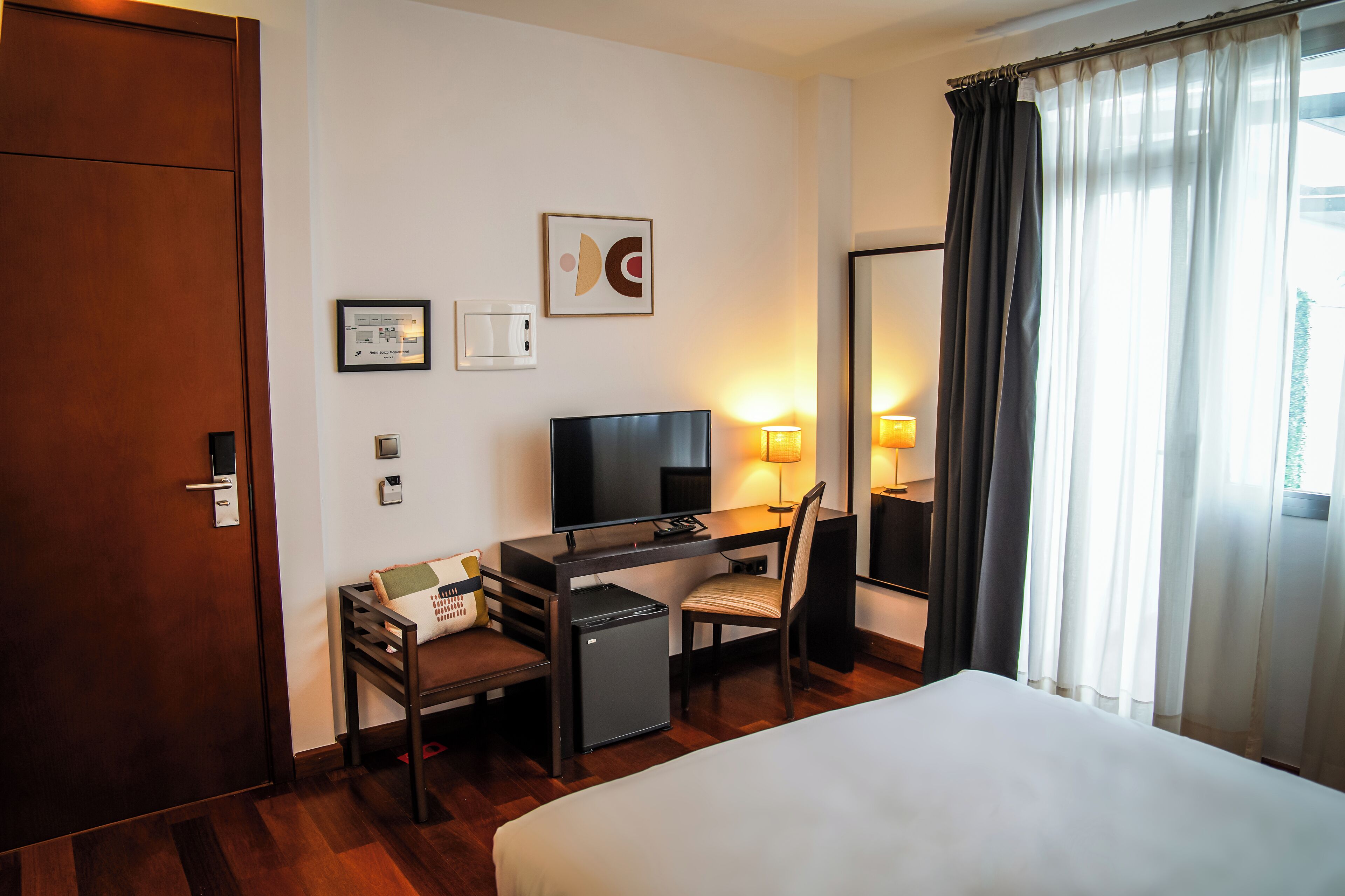 Une chambre d’hôtel équipée d’un lit, d’un bureau, d’une chaise, d’une télévision et d’un petit réfrigérateur.