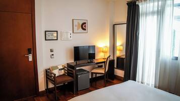 Une chambre d’hôtel équipée d’un lit, d’un bureau, d’une chaise, d’une télévision et d’un petit réfrigérateur.