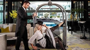 A man pushing a woman in a stylish chair in a modern hotel lobby with a pool view. - Sofitel Auckland Viaduct Harbour (Auckland)