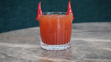 A glass of Bloody Mary with a garnish of red chili peppers on a marble surface.