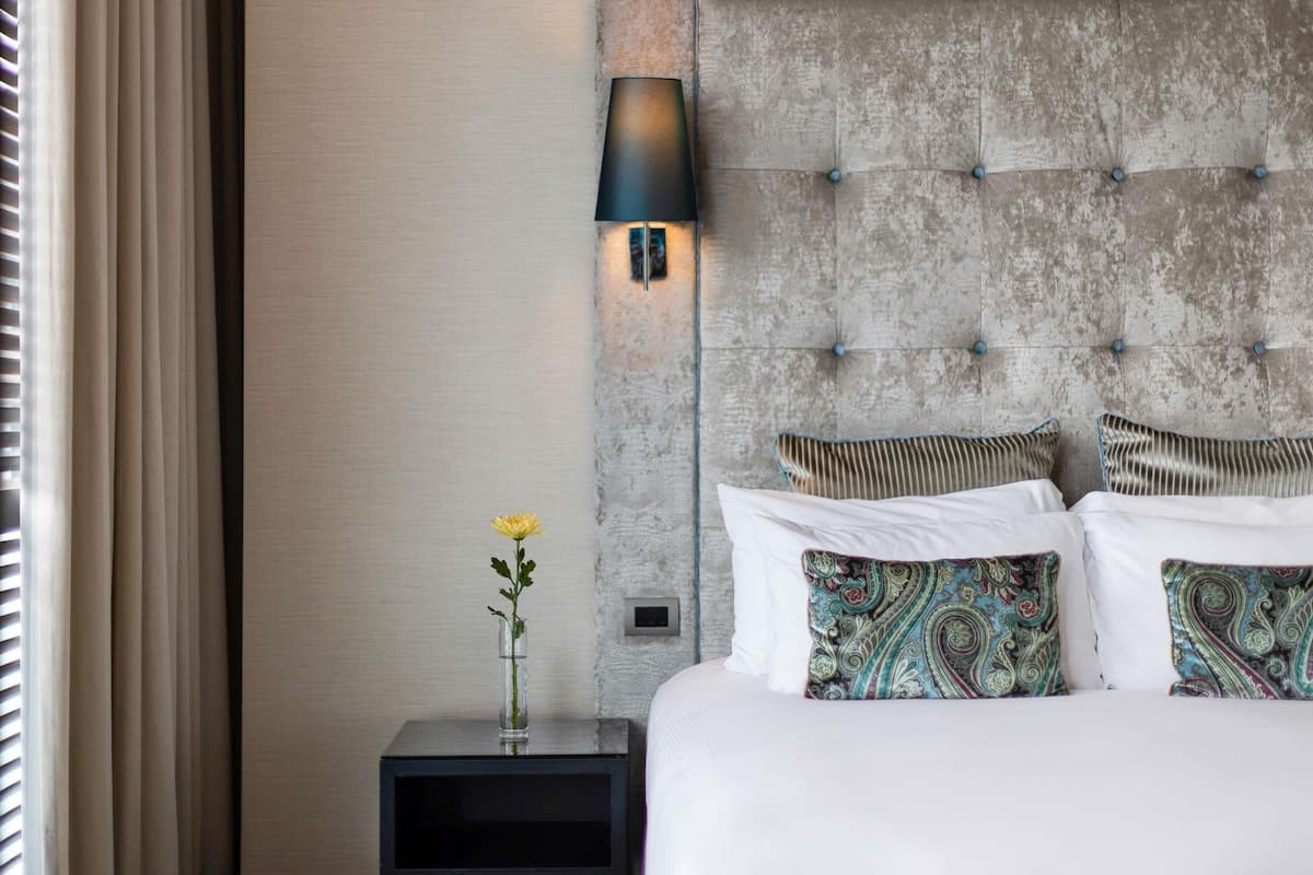 A hotel room with a tufted headboard, a bedside table with a lamp, and patterned pillows.
