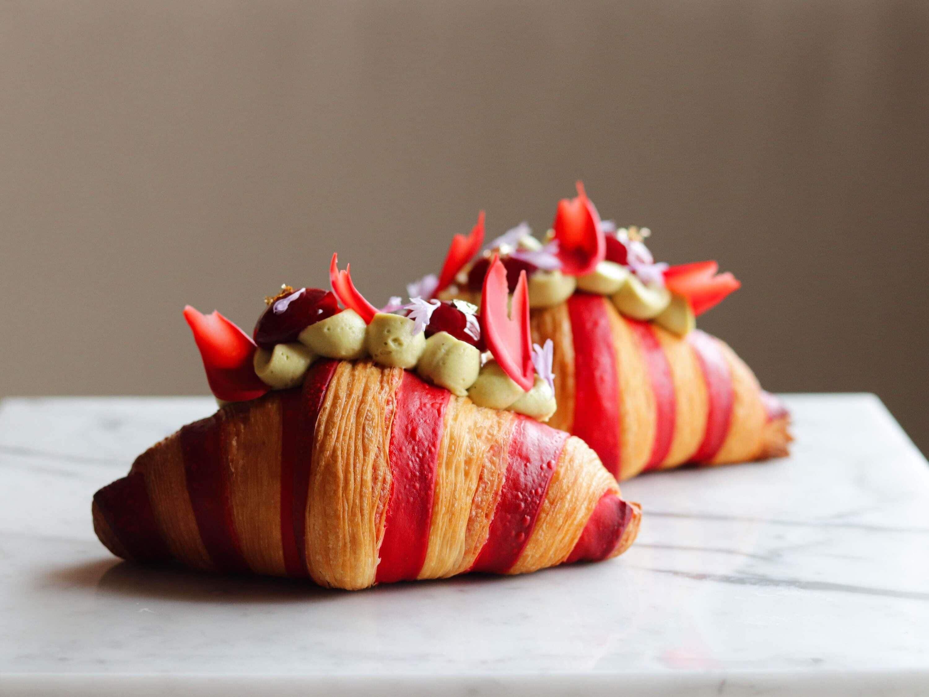 Two croissants with red and white stripes, topped with cream and red flowers, on a marble surface.